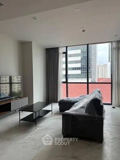 Spacious modern living room with large windows and city view, featuring a sleek sofa and entertainment unit.