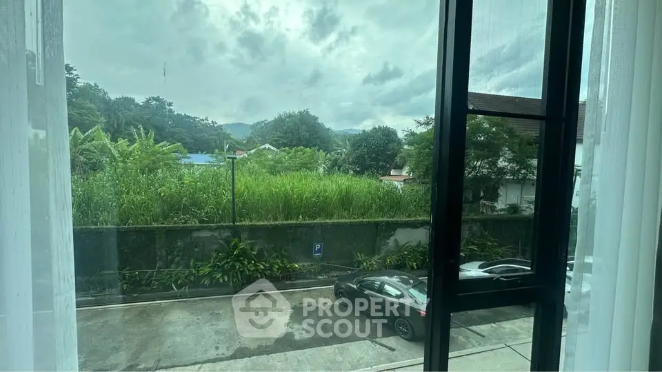 Scenic view from window overlooking lush greenery and parked cars on a cloudy day.