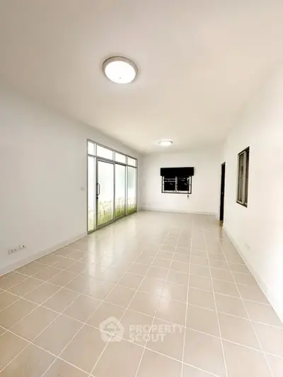 Spacious empty living room with large windows and tiled flooring, perfect for customization.