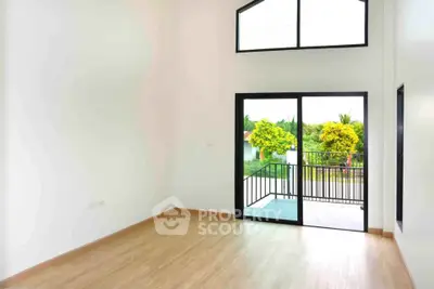 Spacious room with high ceiling and large windows opening to a balcony with garden view.