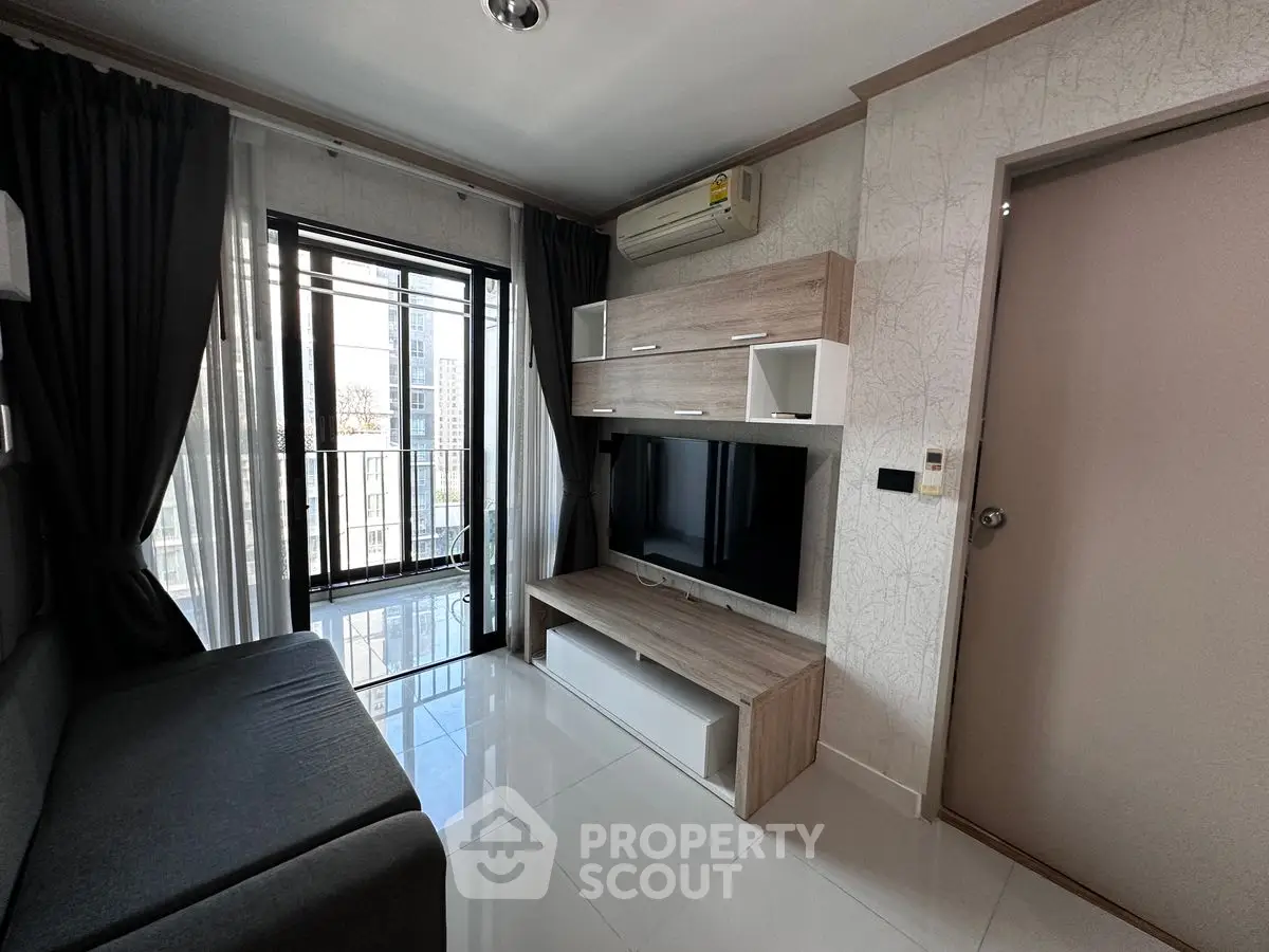 Modern living room with sleek furniture and large TV, featuring a balcony view.