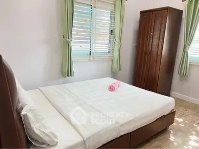 Cozy bedroom with natural light, featuring a comfortable bed and wooden wardrobe, perfect for relaxation.