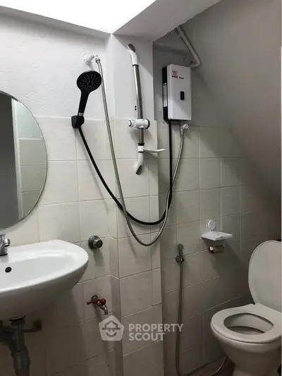Compact bathroom with shower, sink, and toilet under sloped ceiling.
