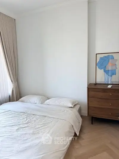 Cozy minimalist bedroom with natural light and stylish wooden dresser.