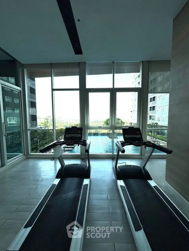 Modern gym with treadmills and pool view in luxury apartment building.