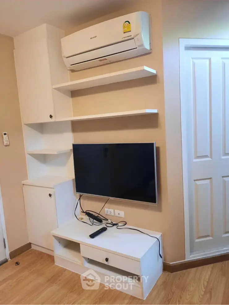 Modern living room with wall-mounted TV and air conditioning unit, featuring sleek storage solutions.