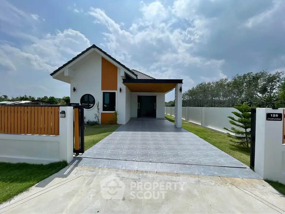 Modern single-story house with spacious driveway and lush greenery under a clear sky.