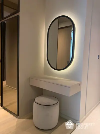 Elegant modern vanity area with illuminated mirror and plush stool in a stylish interior.