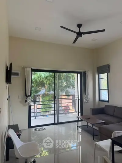 Spacious living room with large windows and balcony access, featuring modern furniture and ceiling fan.