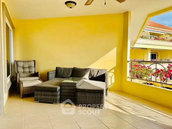Spacious sunny balcony with cozy outdoor seating and vibrant flowers.