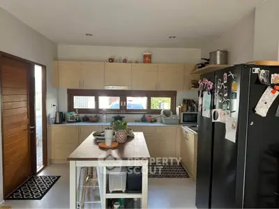 Modern kitchen with island, wooden cabinets, and black fridge in cozy home setting.