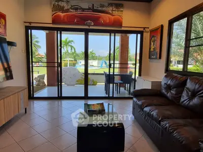 Spacious living room with leather sofa and glass doors opening to a lush garden view.