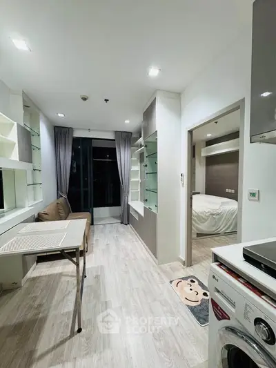 Modern apartment interior with open living area and bedroom, featuring sleek design and ample natural light.
