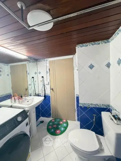 Charming bathroom with wooden ceiling and modern appliances, featuring a washing machine and stylish decor.