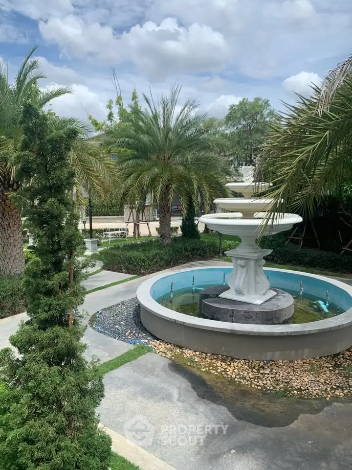 Luxurious garden with elegant fountain and lush palm trees under a clear blue sky.