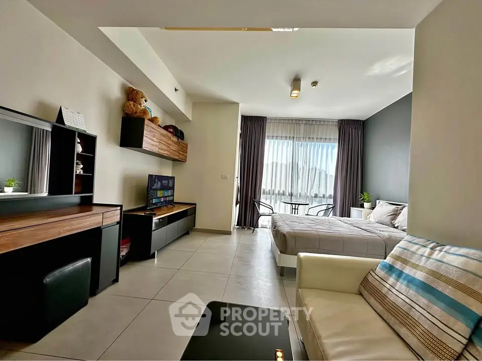 Modern studio apartment with open layout, stylish furnishings, and large window offering natural light.