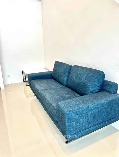 Modern living room with stylish blue sofa and sleek side table on glossy tiled floor.