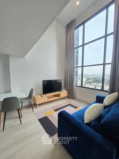 Modern living room with large window and stylish furniture offering city views.