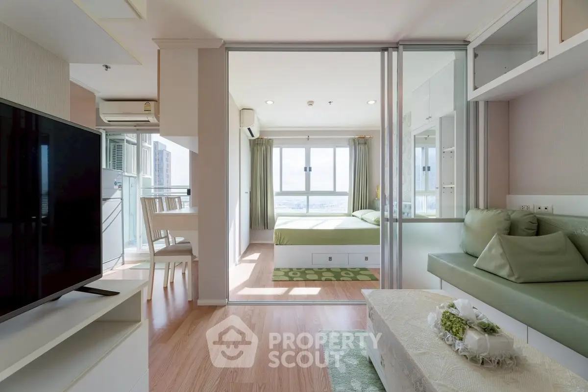 Modern open-plan living room with a view into a stylish bedroom, featuring sleek furniture and natural light.