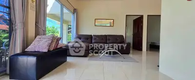 Spacious living room with modern leather sofa and large windows offering garden views.