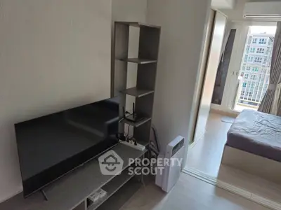 Modern apartment interior with TV, shelving, and a glimpse of the bedroom and balcony view.