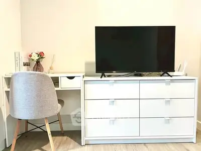 Modern study area with sleek desk, chair, and TV on white dresser.