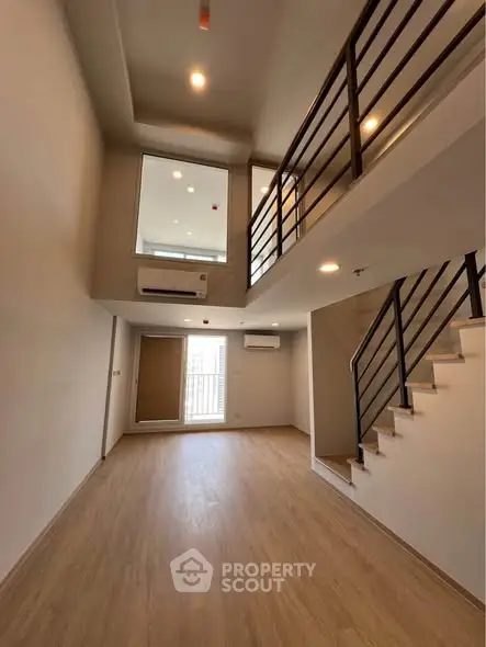 Spacious modern living room with high ceiling and mezzanine, featuring sleek staircase and wooden flooring.