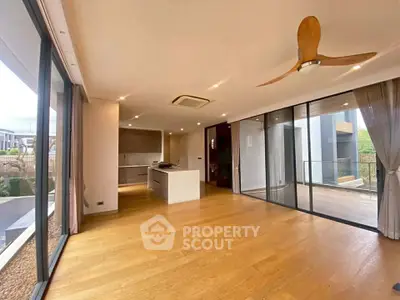 Spacious modern living room with wooden flooring and large windows opening to a balcony.