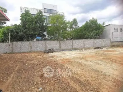 Vacant land plot with potential for development, surrounded by trees and adjacent to a modern building.