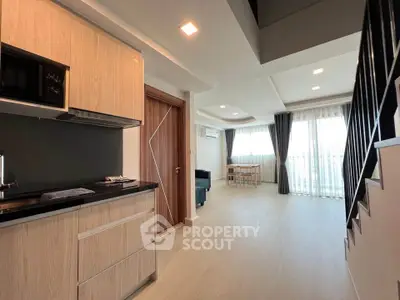 Modern open-plan living room with kitchen and staircase, featuring natural light and sleek design.