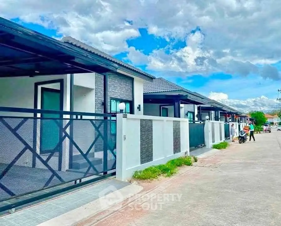 Modern row of stylish single-story homes with sleek design and spacious driveways under a bright blue sky.