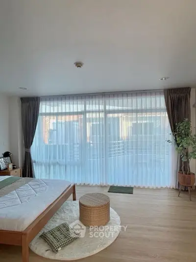 Spacious bedroom with large windows and elegant curtains, featuring a cozy bed and stylish decor.