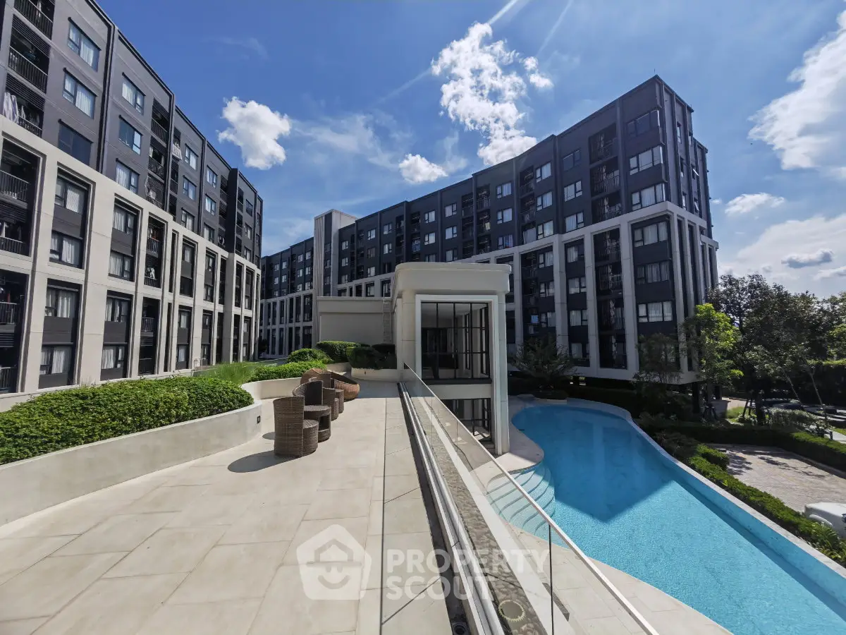 Modern apartment complex with pool and spacious outdoor area under a clear blue sky.