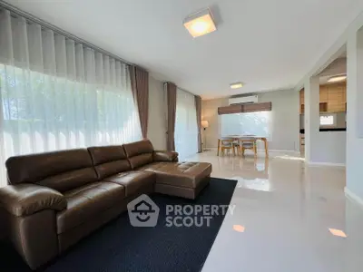 Spacious modern living room with leather sofa and dining area, featuring large windows and elegant decor.