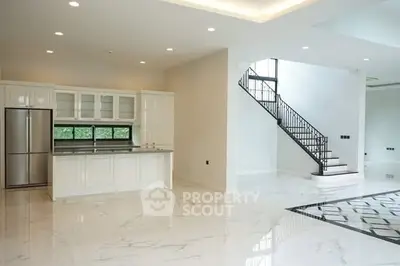 Spacious modern kitchen with sleek design and elegant staircase in luxury home.