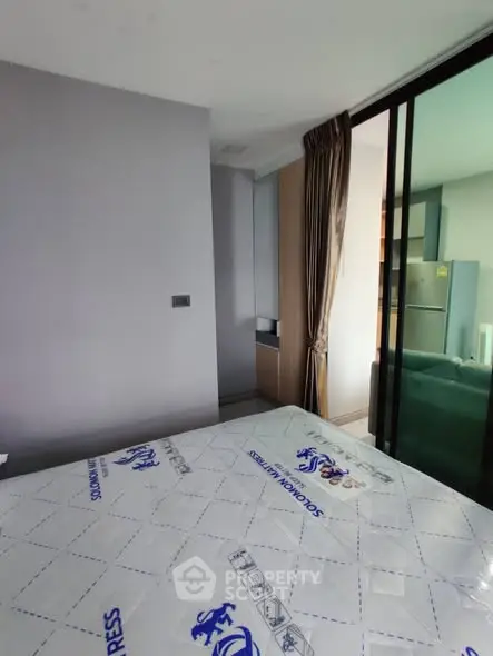 Modern bedroom with sliding glass door and view into kitchen area, featuring sleek design and natural light.