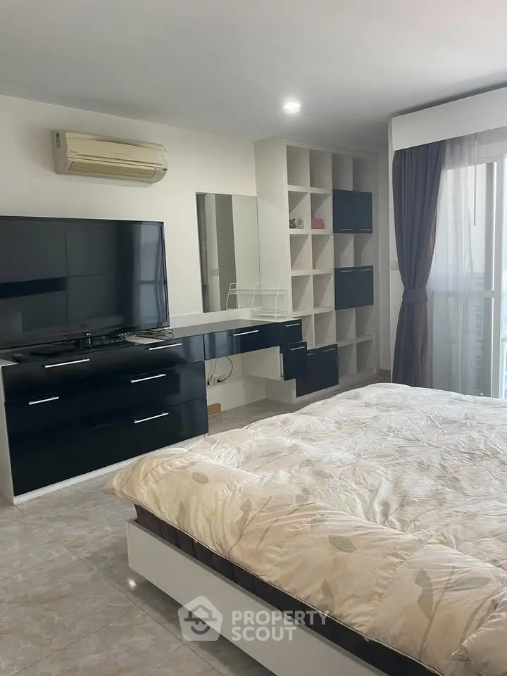 Spacious bedroom with modern furniture and large TV, featuring ample natural light and stylish decor.