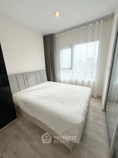 Modern bedroom with large window and city view, featuring a comfortable bed and stylish decor.