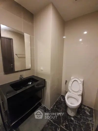 Modern bathroom with sleek black sink and marble flooring in a contemporary apartment.