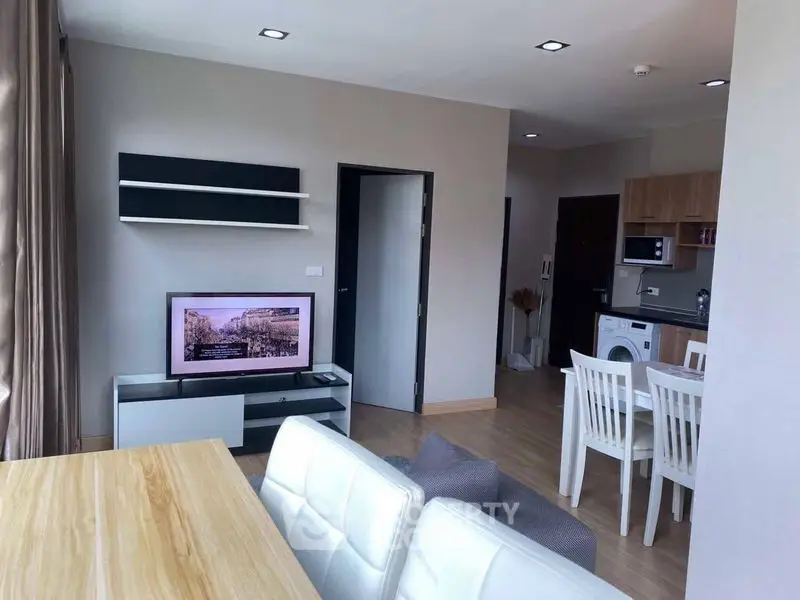 Modern living room with open kitchen and dining area, featuring sleek furniture and a washing machine.