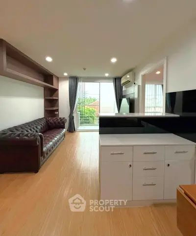 Modern living room with sleek design, featuring a leather sofa and open kitchen layout, leading to a balcony view.