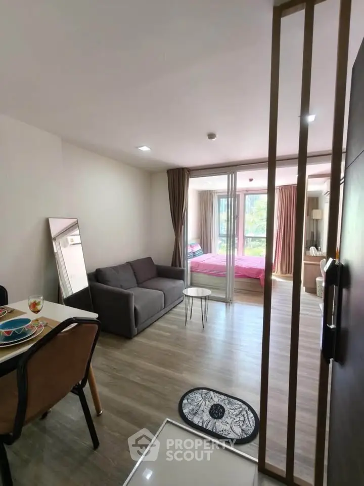 Modern open-plan living room with cozy seating and stylish decor, leading to a bright bedroom with large windows.