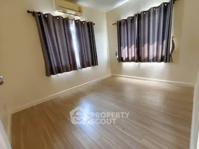 Spacious empty room with wooden flooring and large windows, perfect for customization.