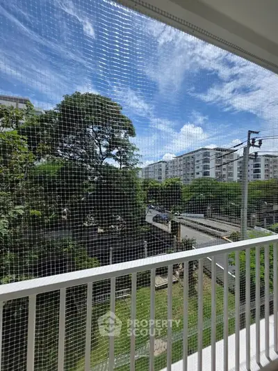 Spacious balcony with safety netting offering a serene view of lush greenery and modern buildings.
