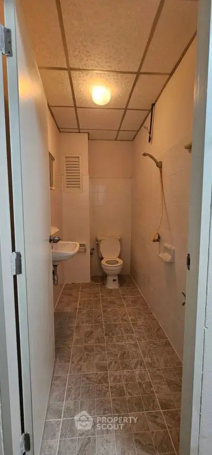 Compact bathroom with tiled floor and shower area, ideal for small spaces.