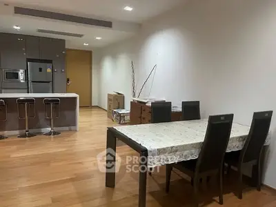 Spacious dining area with modern kitchen and wooden flooring in open layout apartment.