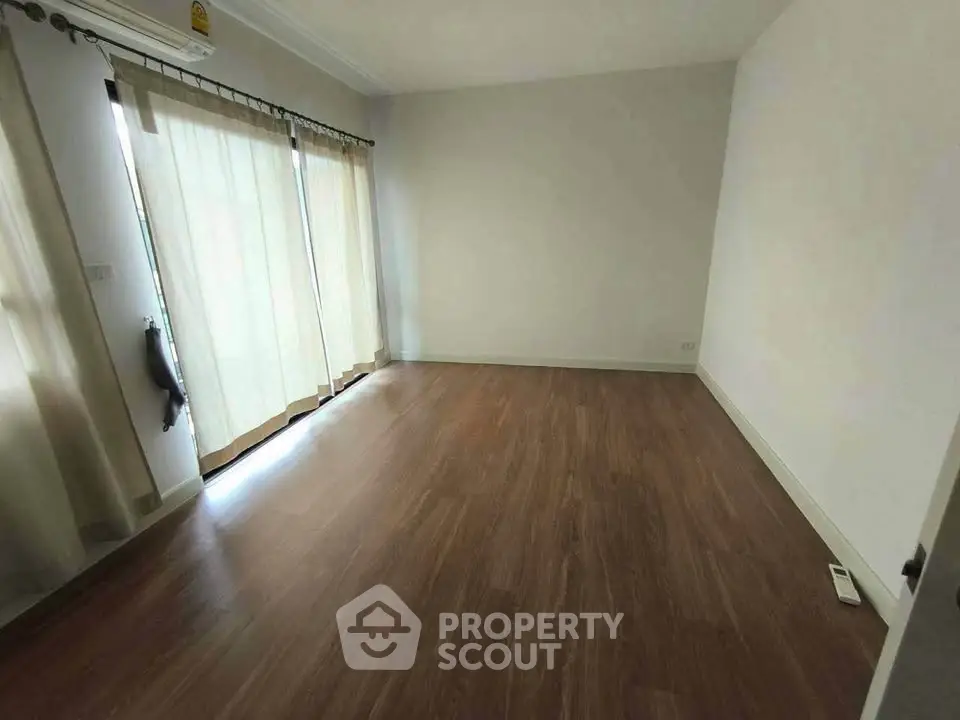Spacious empty room with wooden flooring and large windows for natural light.