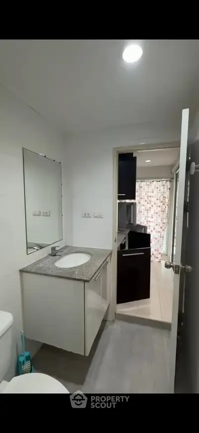 Modern bathroom with sleek vanity and mirror, leading to a stylish kitchen area.
