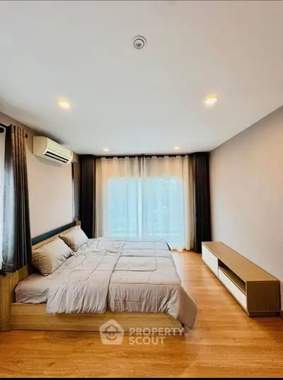 Spacious modern bedroom with wooden flooring and large window for natural light.