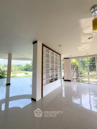 Spacious open-plan living area with large windows and built-in shelving, offering abundant natural light and garden views.